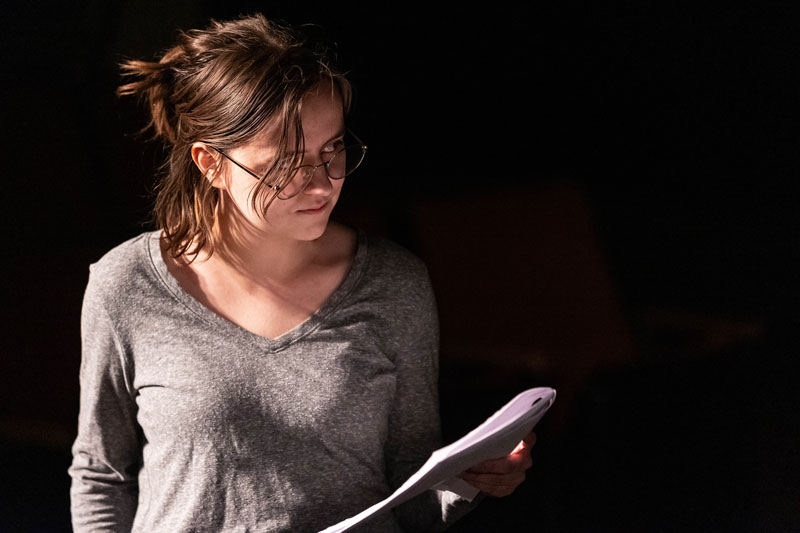 A student actress with a book on stage in darkness