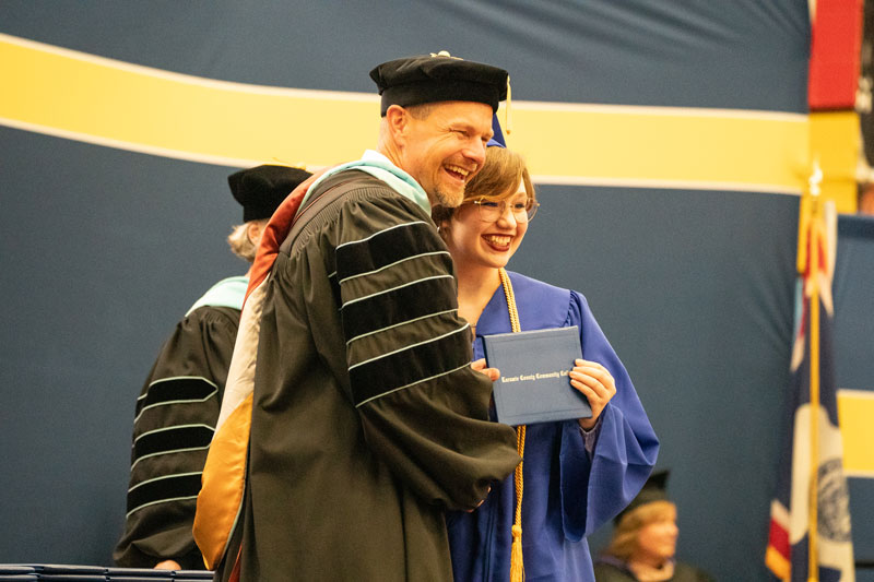 LCCC President Joe Schaffer posing with a graduate on stage during the commencement ceremony in caps and gowns.