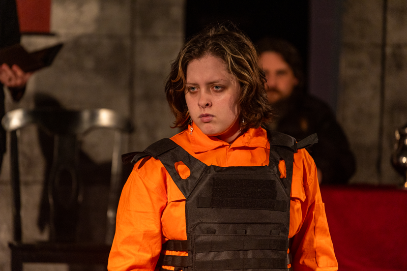 Actress from Antigone on stage in orange suit with vest