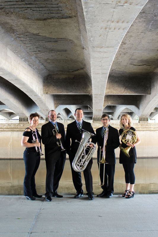 Photo of the Alliance Brass Band with their instruments standing under an overpass