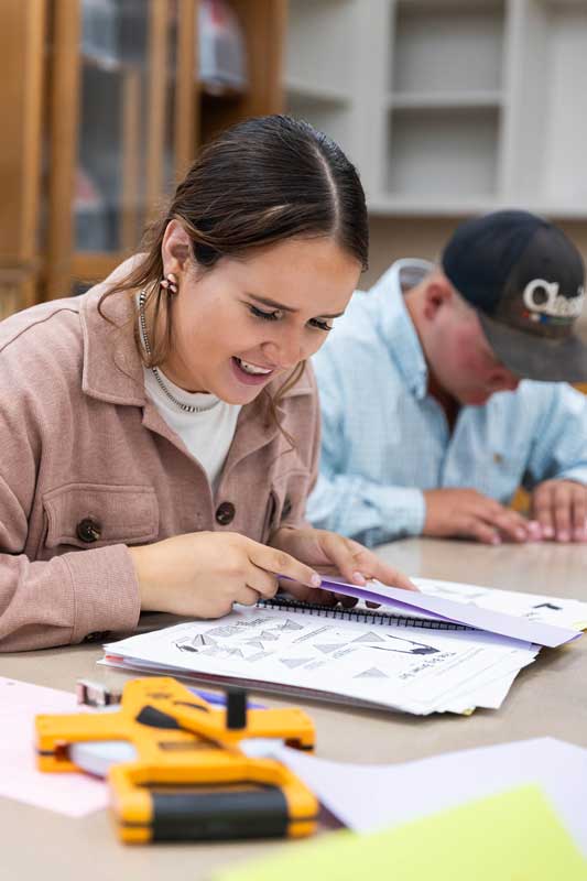 LCCC student Laramie Nutter working in class with notes/papers on the table in front of them and a survey measuring tape