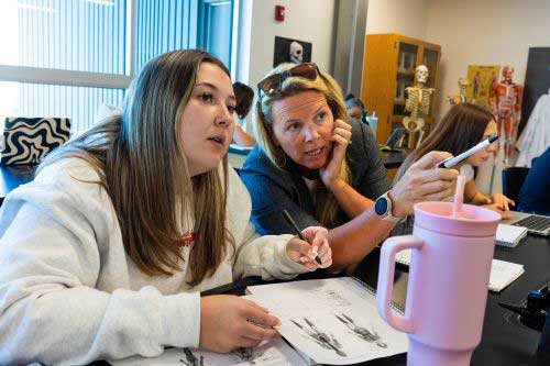 LCCC student Sorinna Meyers talks with faculty member Katie Blunn in class while pointing at information 