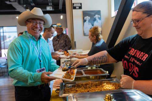 A man smiles at the camera while in line for food at Cheyenne Frontier Days. LCCC Dining Services staff is serving him food.
