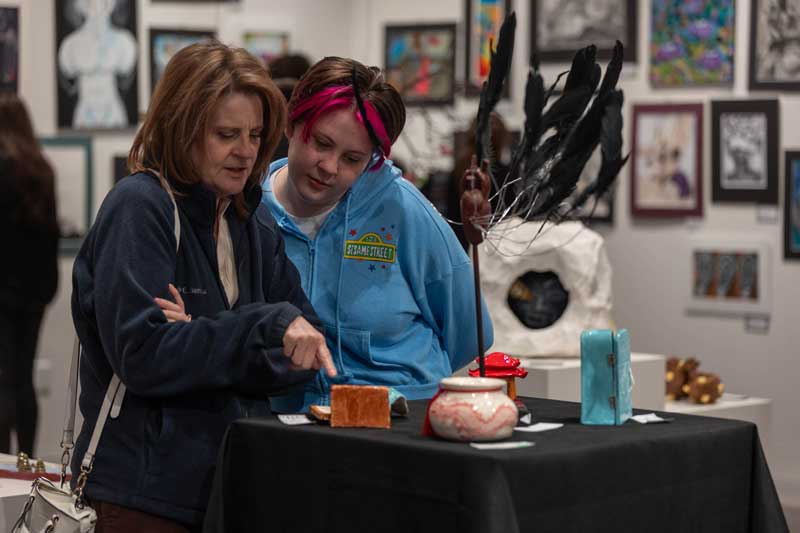 Two people looking at the 3D ceramic art pieces on stands in the middle of the gallery