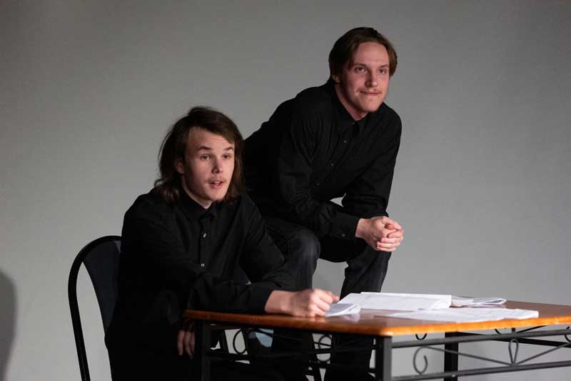 Two student actors on stage sitting at a desk