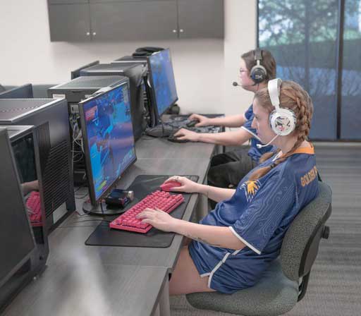 Two Esports athletes competing in jerseys on computers with headsets