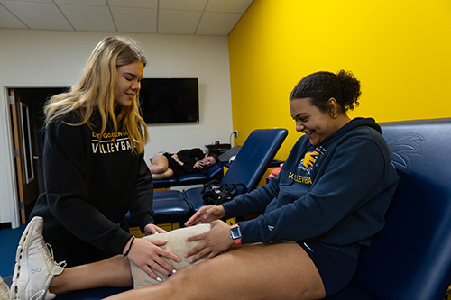 Lea, left, and Zoe, volleyball athletes at LCCC, examine Zoe’s knee in the athletic trainer’s room. 