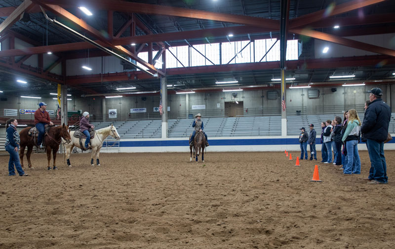 Ag instructor on a horse in the LCCC arena talking to potential students in a line on the right with two students on horses on the left.