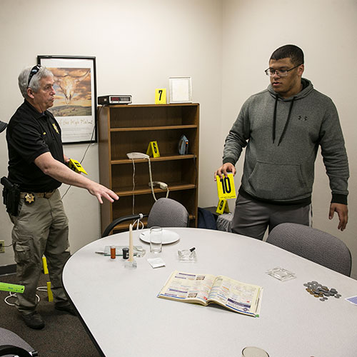 sheriff working with students to mark evidence in a mock crime scene