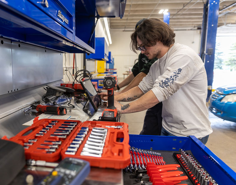 Photo of auto tech student standing at a table with many tools and a computer.