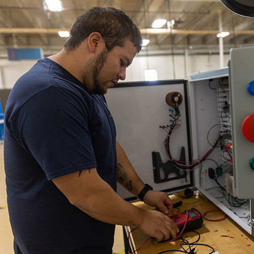 student using tool to measure electrical output of wires in a wiring cabinet in class