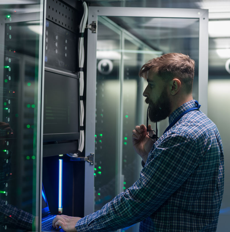 photo of a man working on a laptop by servers