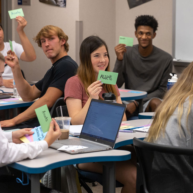photo of a group of students in class holding up cards with "assets" written on them.