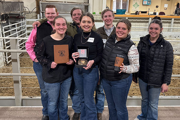 Posed photo of the Livestock Judging Team with awards in front of livestock pens.