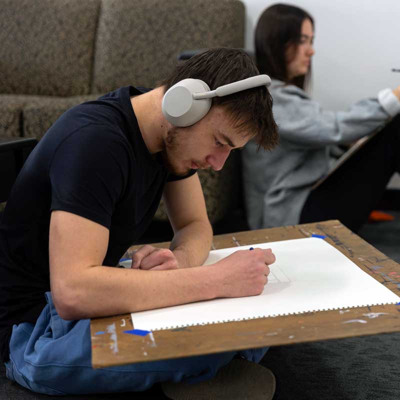 student drawing in the hallway with headphones on