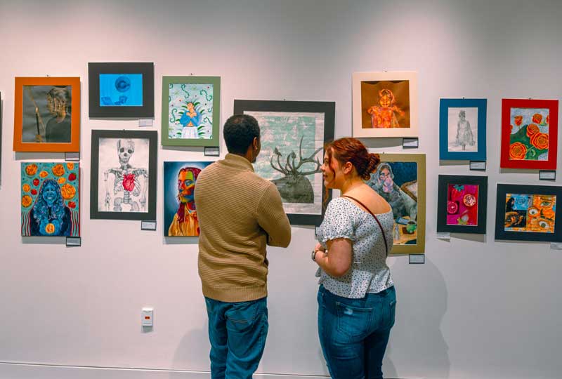two people looking at 2D student art on the walls in the gallery