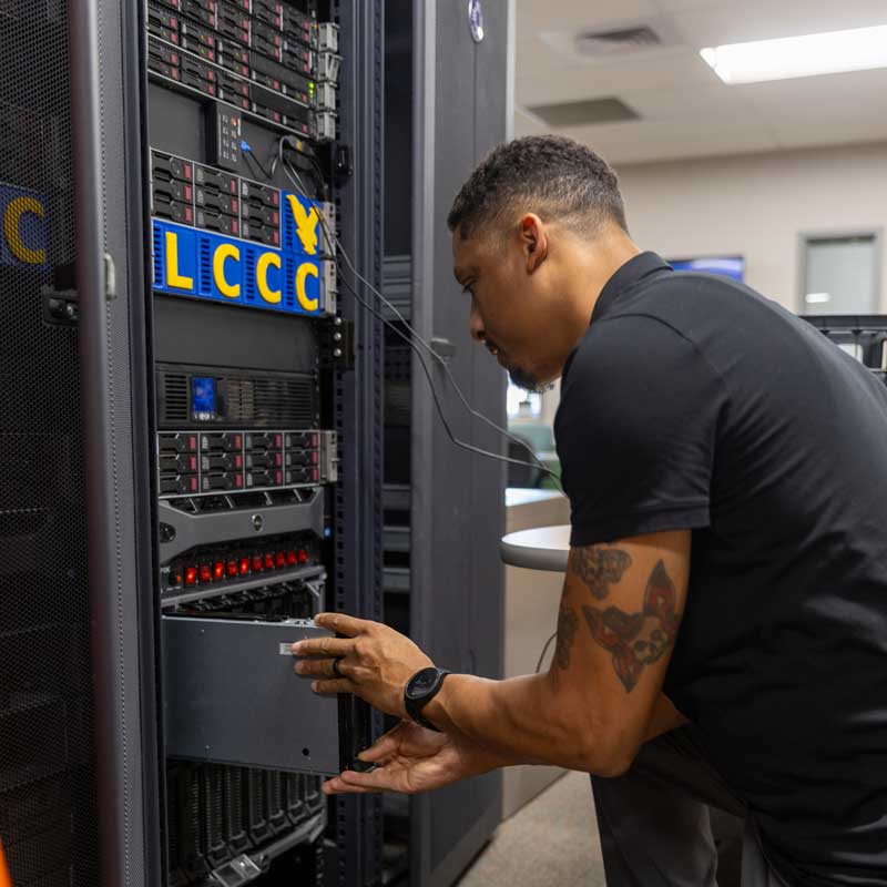 A student putting in computer components in a server rack.