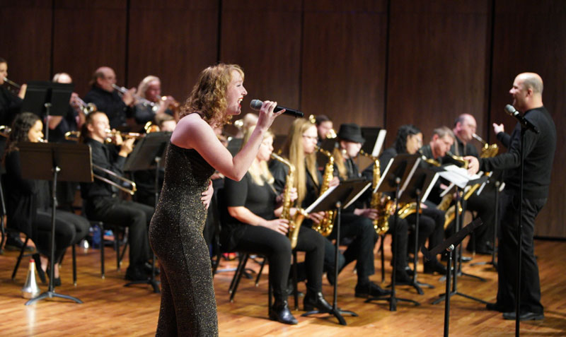 photo of woman singing on stage with a band behind her