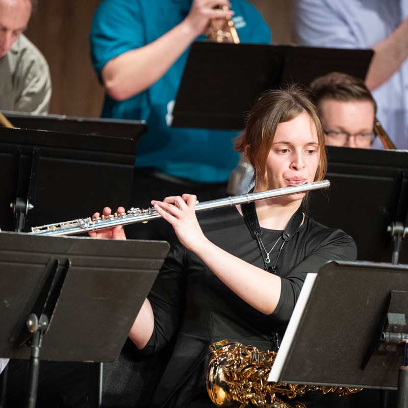 student playing the flute on stage during a concert surrounded by other musicians