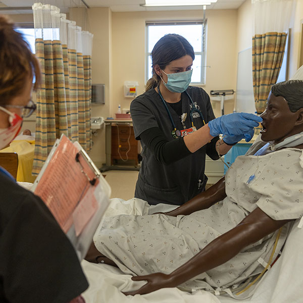 Nursing student working on simulator patient with faculty member watching