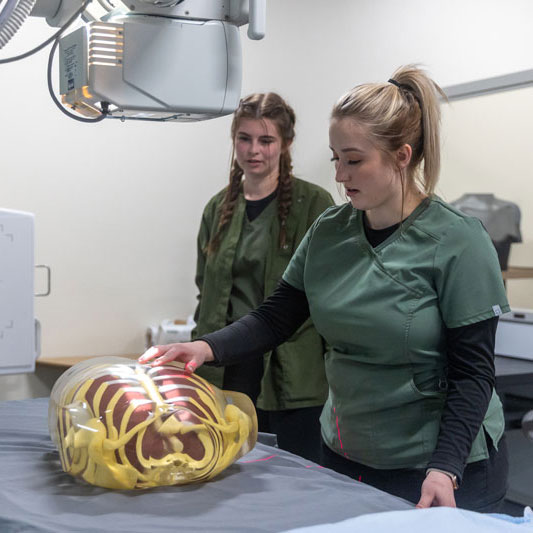 Students positioning a practice chest under x-ray machine.