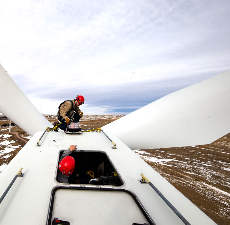 photo of a student on top of a wind turbine in helmet and harness