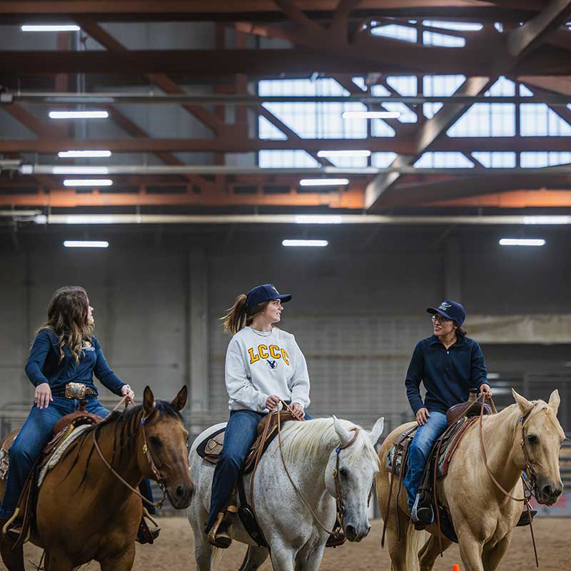 Three students riding horses in a row in the LCCC Arena