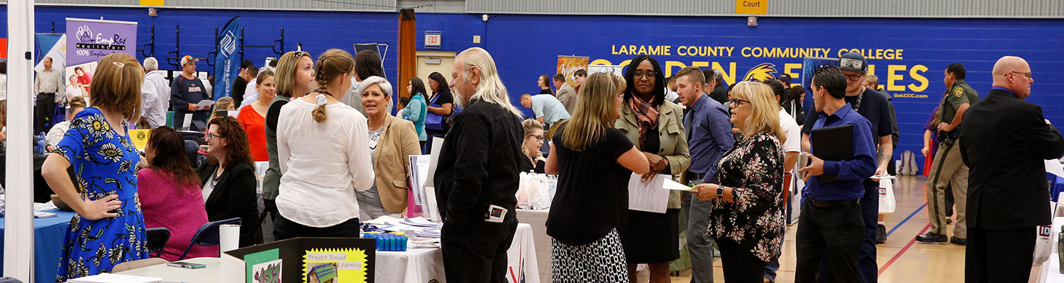 photo of a crowd of people standing in the LCCC multipurpose gym during a career fair. There are tables with employers at them, and people standing talking with them.