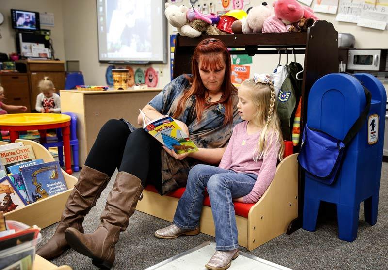 CDC staff member Beth Storer reads one-on-one with a young girl. They are seated together on a low bench.