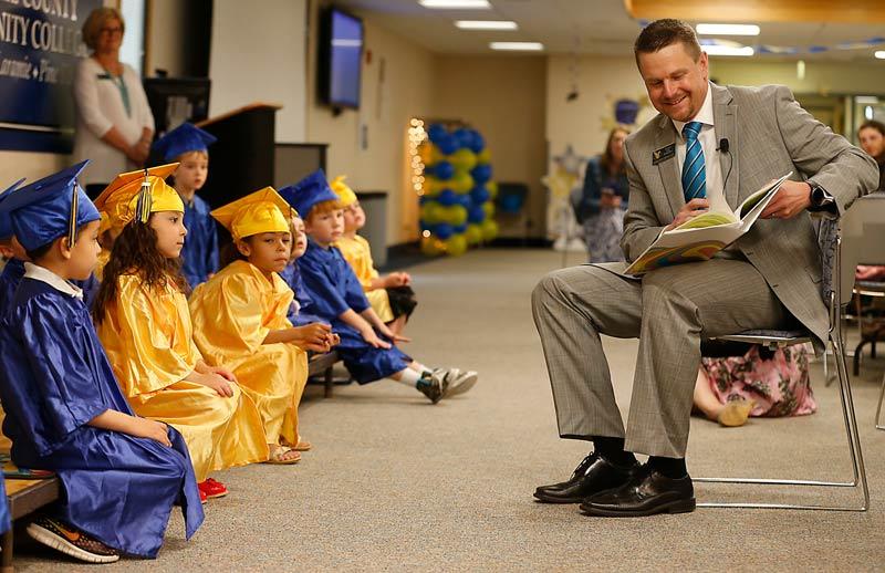 LCCC President Dr. Schaffer reads a book to a group of CDC students dressed in caps and gowns for their preschool graduation
