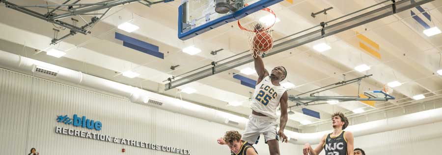 An LCCC basketball player dunking the ball during a game with defenders around him.