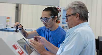 Photo of two people looking into a CNC machine and talking