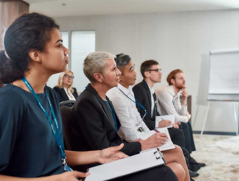 photo of a group of people in a training looking forward with notepads on their laps and a big tablet of paper off to the side