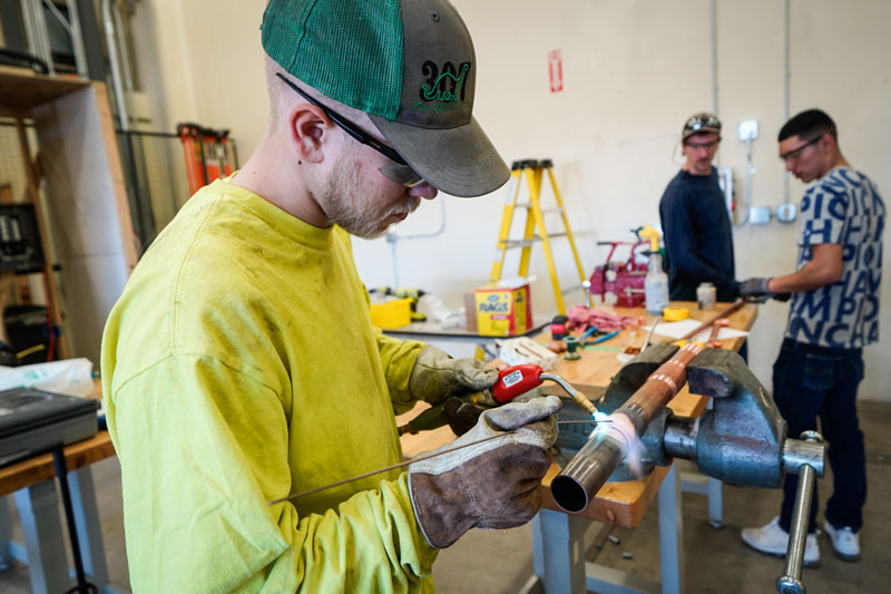 photo of a man soldering a pipe with two more in the background