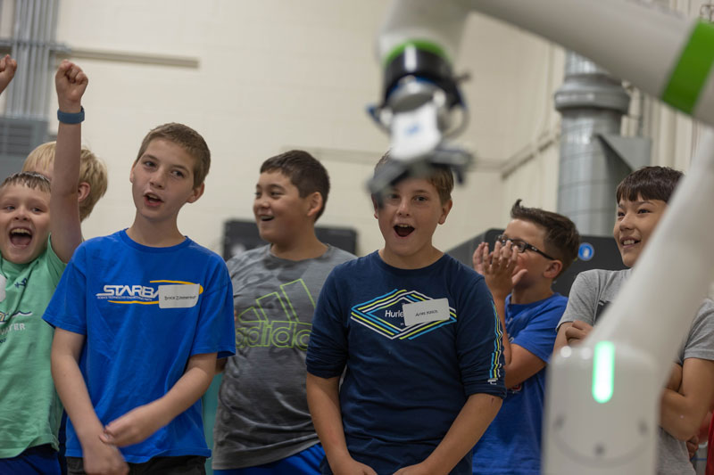 photo of kids looking at a robotic arm and cheering