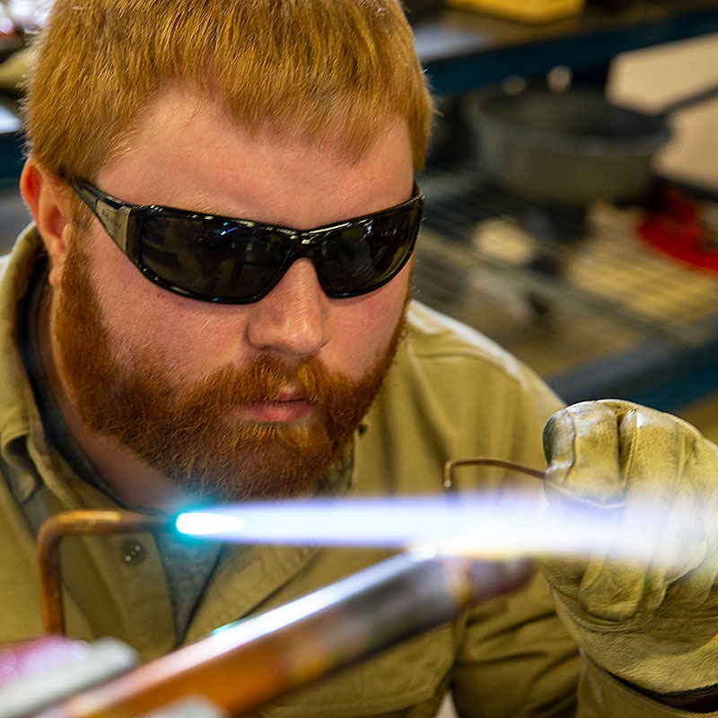 Male student welding with a torch and pipe. 